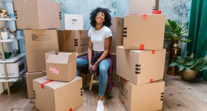 Photograph of a Woman in a White Shirt Sitting Beside Cardboard Boxes